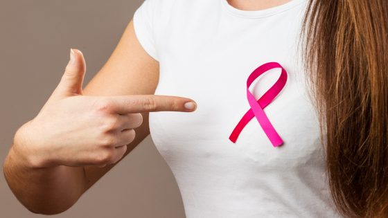 Healthcare, medicine and breast cancer awareness concept. Woman in t-shirt with pink cancer ribbon pointing